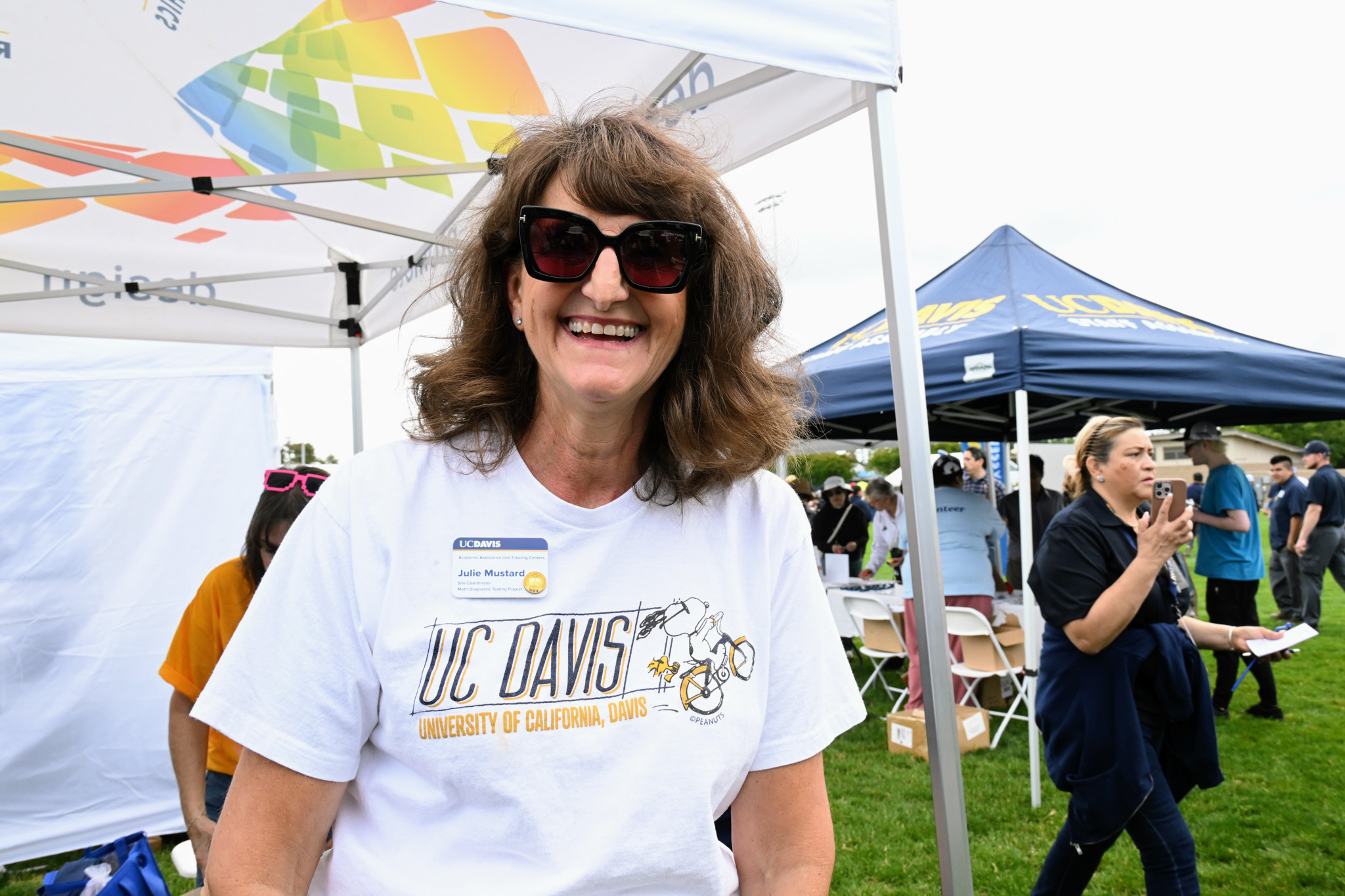 Smiling woman in sunglasses wearing a UC Davis t-shirt at an outdoor fair