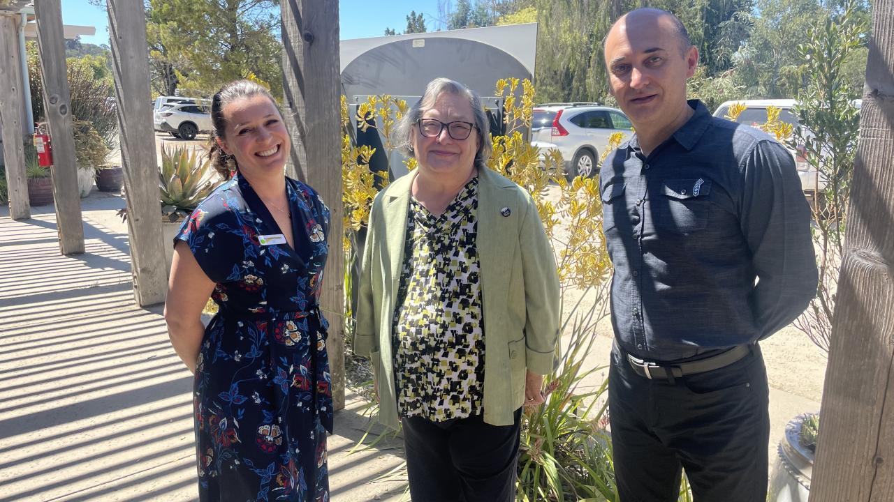 Photo of three people standing outside on a sunny day. 