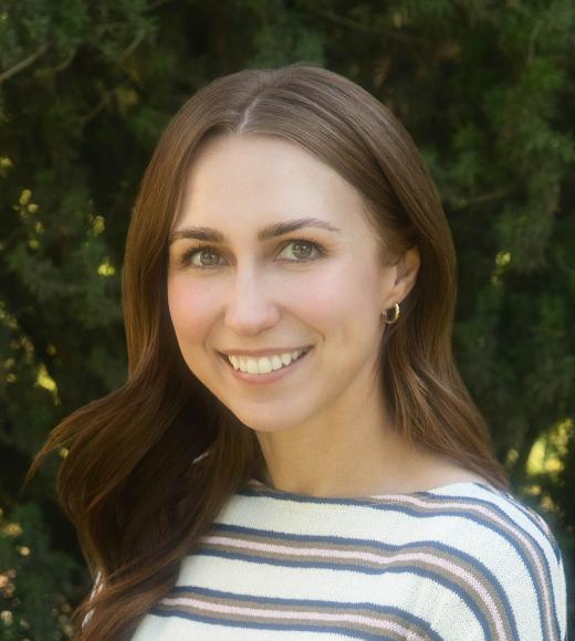 Smiling young woman with long brown hair, striped top, leafy green background